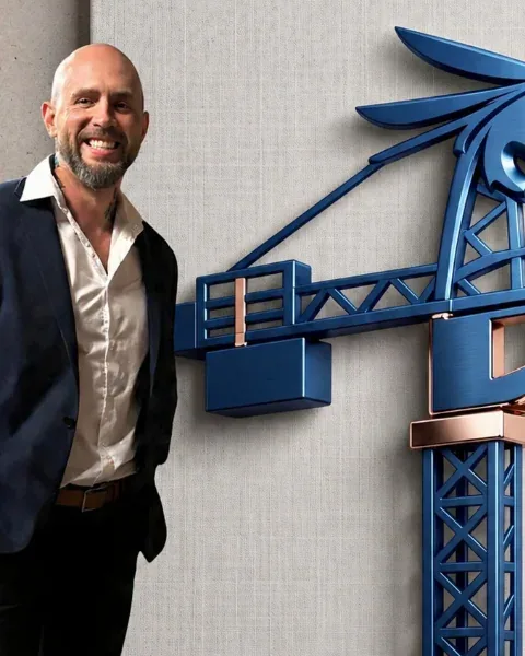 Trevor Stuckless, smiling, standing beside the Blue Crane Works crane sculpture